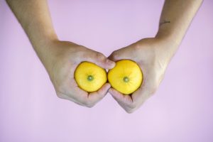 Two hands holding lemons that seem to look like a pair of breasts.